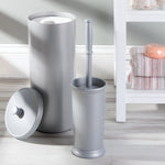 Silver toilet brush and matching tall cylindrical container with a separate lidded canister and folded towels on a shelf nearby.