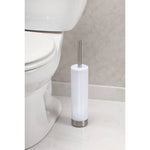 iDesign white toilet brush and holder with brushed stainless handle placed on a bathroom floor next to a toilet