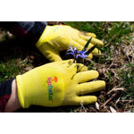Close-up of yellow-green kids gardening gloves on grass with small blue flower, showing textured coating and logo