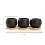 Three textured black mini cement pots on a bamboo tray with dimension lines indicating width and height on white background.