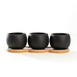 Three round textured black mini cement planters arranged on a contoured bamboo tray against white background.