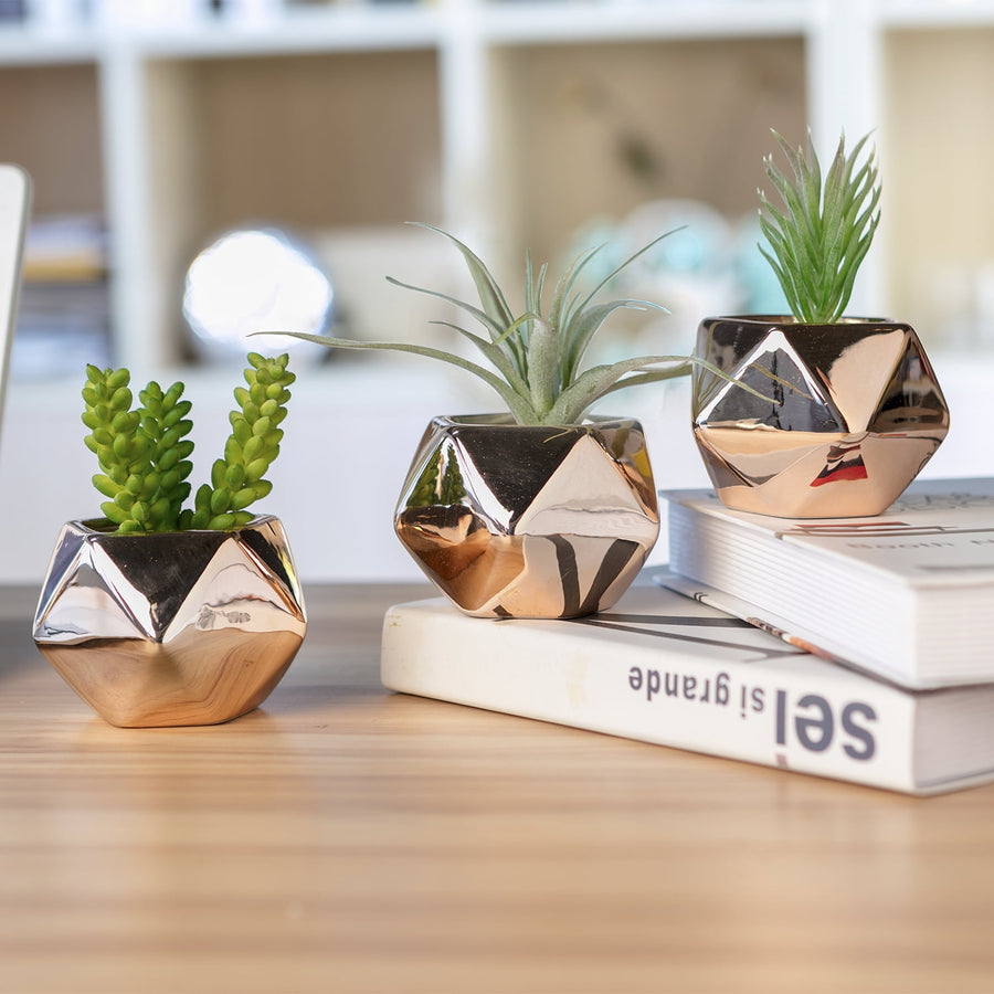 Three glossy copper geometric succulent planters staged on a wooden surface with small faux succulents