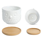 K‑Cliffs white owl planter shown upright and the smaller pot shown on its side revealing a drainage hole, with two bamboo saucers.