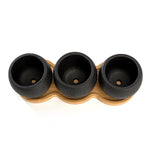 Top-down view of three round black textured mini planters seated in matching contoured bamboo tray showing interior drainage holes.