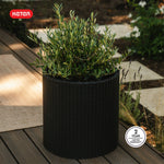 Keter-branded graphite rattan cylinder planter with leafy plant on a deck and a '2 year limited warranty' badge