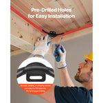 Person installing red PEX pipe into a black pre-drilled bend support under a wooden joist