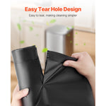 Hands tearing a black trash bag at a perforated tear hole with kitchen trash can blurred in background