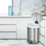 Kitchen scene with stainless steel step trash can lined with a light trash bag and Great Value product boxes on the counter