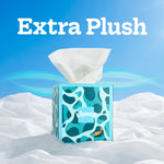 Kleenex cube tissue box on a crumpled white surface against a blue gradient background with 'Extra Plush' text