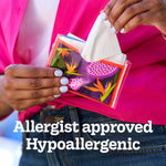 Close-up of hands pulling a tissue from a Kleenex slim wallet pack with fruit-and-floral design and 'Allergist approved' text