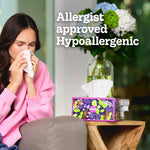 Woman on a couch blowing her nose beside a decorative Kleenex tissue box with 'Allergist approved Hypoallergenic' text.