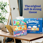 Stacked colorful Kleenex tissue boxes and large Trusted Care carton on a desk with slogan text