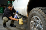 Person kneeling and cleaning a truck step while holding a GUNK degreaser spray bottle and rag