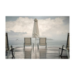 Lakeside dock with two lounge chairs and a closed umbrella on a wet wooden deck in overcast weather