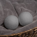 Two gray wool dryer balls resting on a folded gray towel inside a woven basket, product styling