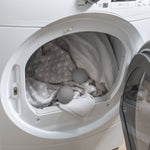 Two gray wool dryer balls inside a front-load dryer with towels and linens, lifestyle context