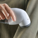 Hand-held demonstration of a white Laundry 360 lint remover being used on a fabric surface, showing tool contact with cloth