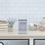 Lifestyle scene of a laundry room countertop featuring a box of Mrs. Meyer's Lavender dryer sheets with decorative lavender and towels