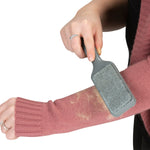 Hand using a gray lint-removing brush to remove fuzz and hair from a pink sweater sleeve