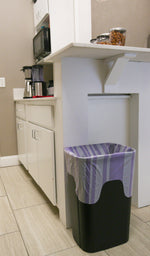 Lavender-striped trash bag liner fitted over a rectangular kitchen waste bin under a counter in a kitchenette