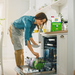 Woman loading a dishwasher with a Lemi Shine Dishwasher Pacs bag on the counter in a bright kitchen