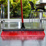Libman 24-inch push broom with red bristles positioned on a polished indoor floor in a room setting