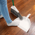 Person using a Libman angle broom to sweep debris into a white dustpan on a hardwood floor