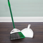 Libman angled broom and white dustpan set with green handle positioned on a dark wood floor against a light wall.