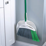 Libman angled broom nested in white dustpan, leaning against a wall with green handle visible