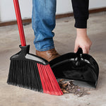 Person using Libman red-handled angle broom to sweep debris into a black dustpan on concrete floor