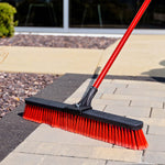 Red-handled Libman push broom angled to clean between pavers and hardscape edging outdoors