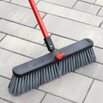 Close-up of Libman broom head on pavers showing grey stiff bristles, black plastic head and red adjustment knob.