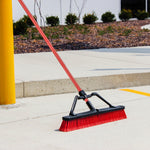 Libman red-handled push broom positioned on outdoor concrete near a curb and landscaping