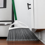 Green-handled Libman angle broom sweeping along a kitchen baseboard beside cabinets and stainless appliance