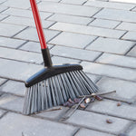Libman outdoor angle broom sweeping small rocks and sticks from a paved surface, showing angled black head and gray bristles