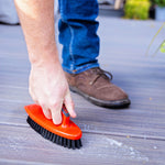 Person scrubbing a deck surface with a red Libman hand brush with black bristles