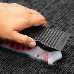 Hand using a black Libman scrub brush to work foam into a dark carpeted surface