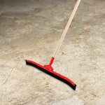 Red curved floor squeegee with black rubber blade and wooden handle positioned on textured concrete floor