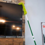 Green microfiber duster on an extended pole reaching the top corner of a mounted flat panel TV
