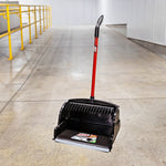 Black upright scoop dustpan with red handle positioned in an industrial corridor, label visible on pan floor.