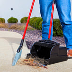 Close view of black upright scoop dustpan and red-handled broom collecting hair and debris on a sidewalk.