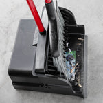 Top-down view of a black upright scoop dustpan holding small debris with a red-handled broom resting against it.
