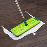 Green Libman flat mop head on a hardwood floor wiping up a white liquid spill