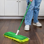 User holding green-handle mop with green microfiber refill cleaning a kitchen floor near cabinets