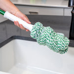 Hand holding Libman mop handle with twisted green-and-white refill over a sink, focusing on mop head and handle grip