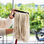 Person holding a Libman mop head clipped into a black plastic mop frame outdoors, showing the clip attachment and hanging yarn strands.