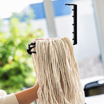 Libman cut-end mop refill clipped to a black plastic attachment held by a person, photographed against a blurred outdoor-background window.