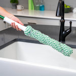 Hand holding a green-and-white Libman twist mop head over a farmhouse sink and faucet