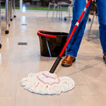 Person mopping a light tile floor with a red-handle mop and white yarn refill, black bucket visible in background