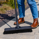 Outdoor lifestyle image of a Libman push broom being used on pavers, showing broom head, handle and lower legs